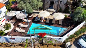 A rooftop pool with lounge chairs and umbrellas, surrounded by trees and a stone building.