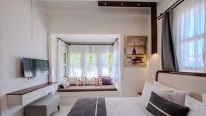 A hotel room with a bed, a bench, a TV, a window with curtains, and a painting on the wall.