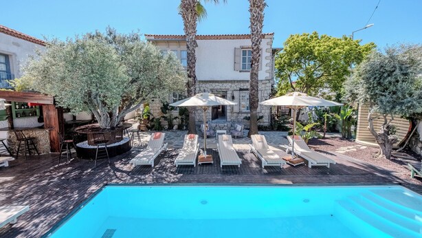 A pool area with lounge chairs and umbrellas, a bar, and a stone building with a tiled roof.