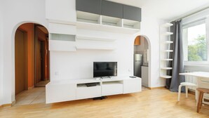 A modern living room with a flat-screen TV, white cabinetry, and a dining area with a table and chairs. - RentPlanet - Studio Anielewicza (Warsaw)