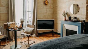 Una habitación con cama, televisión, chimenea, una mesa con alimentos para el desayuno y una ventana con cortinas.