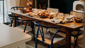 Un comedor con mesa de madera, sillas azules, lámparas colgantes y una ventana con cortinas.