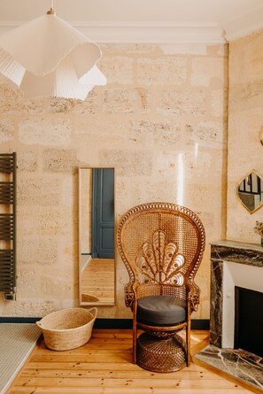 Habitació amb paret de maó rústic, cadira de veta, sòl de fusta, làmpada blanca i mirall que reflecteix una porta blava.