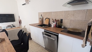 A compact kitchen with a dishwasher, a stove, and a TV mounted on the wall. - Village house in a small hamlet in the heart of the Petite Camargue (Vauvert)
