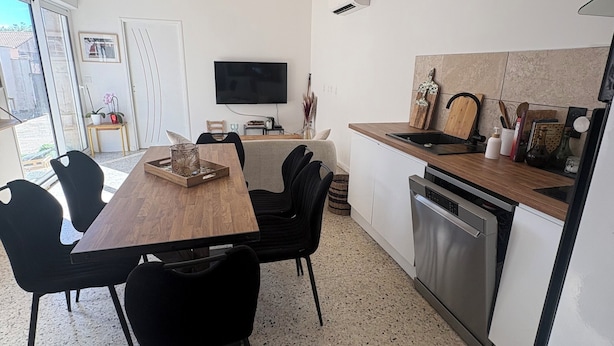 A modern kitchen with a wooden dining table, black chairs, a TV, and a dishwasher. - Village house in a small hamlet in the heart of the Petite Camargue (Vauvert)