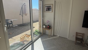 A room with a sliding glass door leading to an outdoor area, a small wooden table with a potted plant, and a framed picture on the wall. - Village house in a small hamlet in the heart of the Petite Camargue (Vauvert)