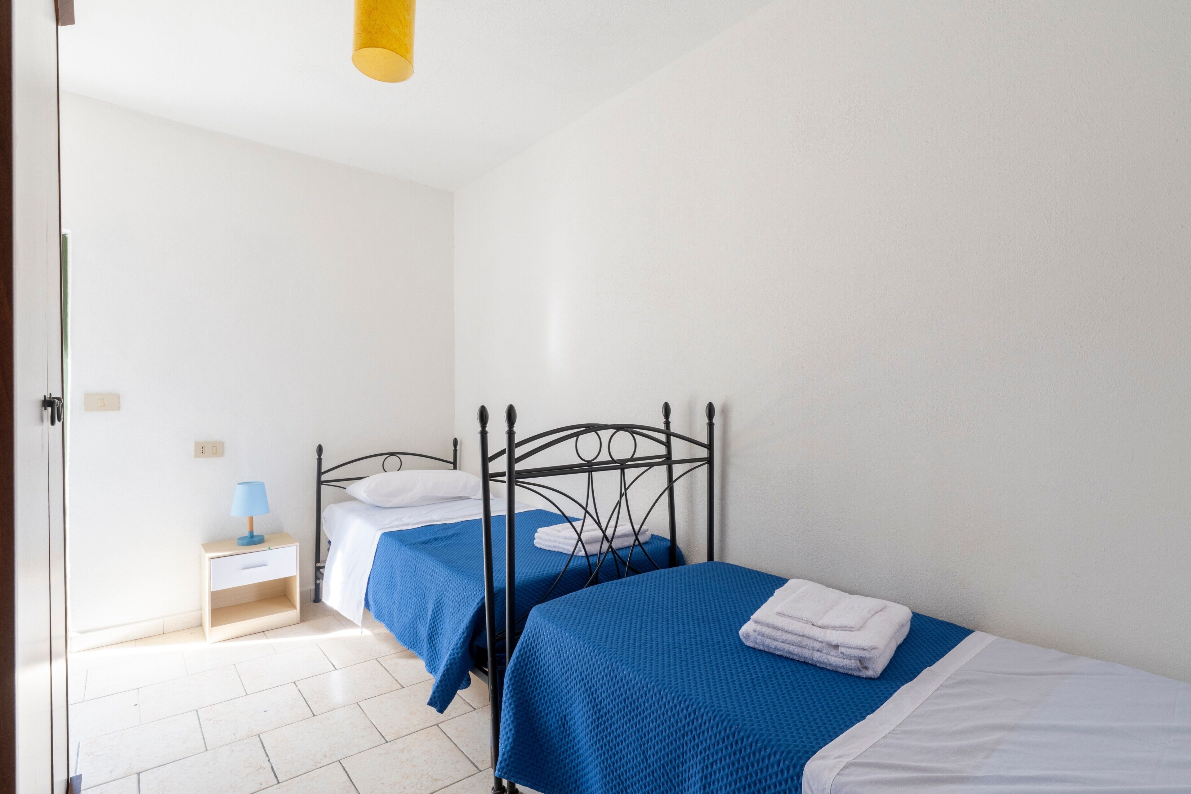 A bedroom with two beds, a nightstand, and a lamp.
