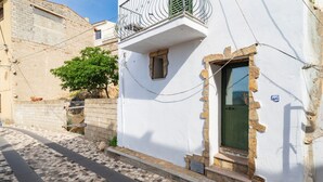 Uma rua de paralelepípedos estreita com um edifício branco, varanda e porta verde.