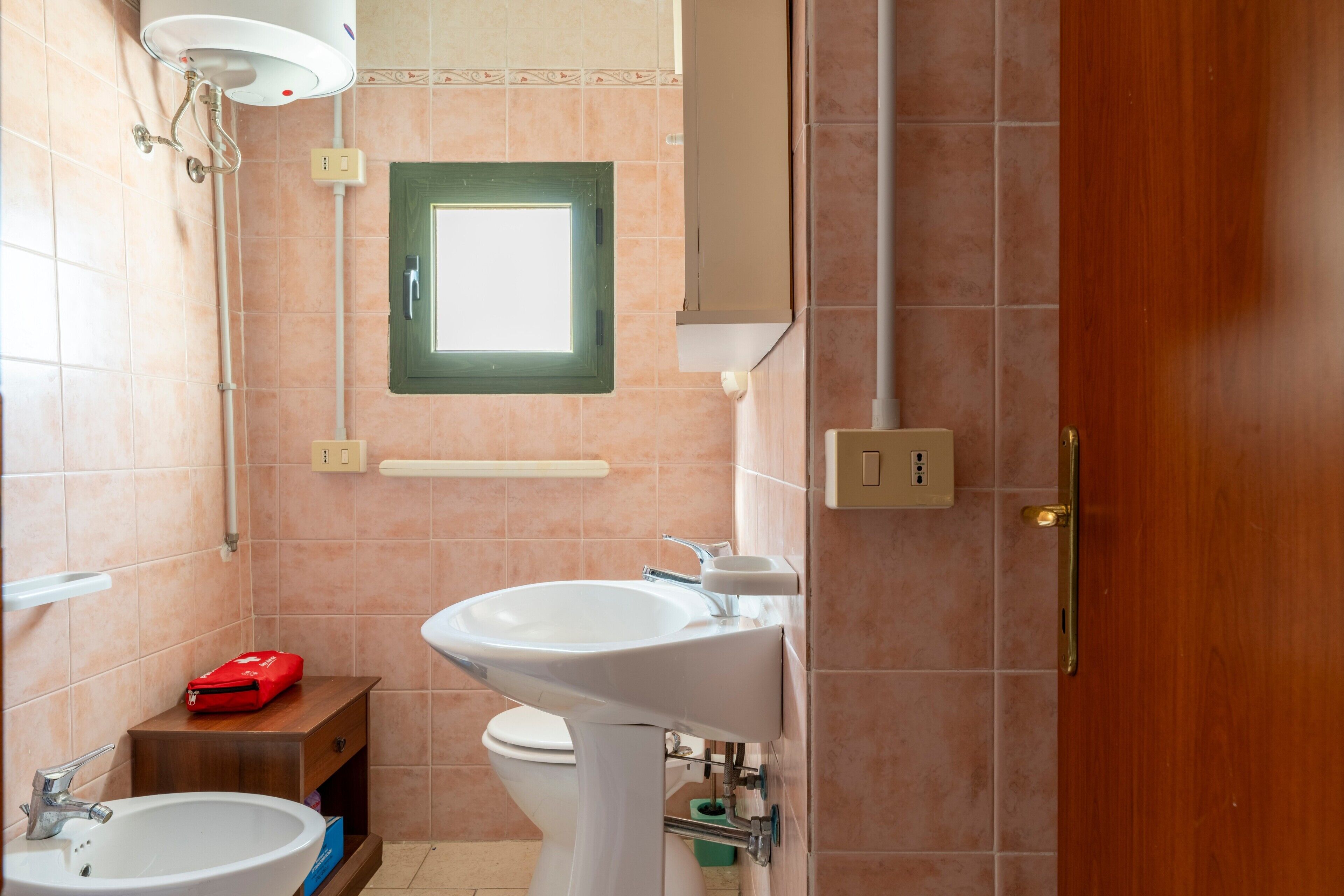 Een badkamer met een wastafel, toilet, douche en een raam.