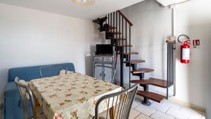 Uma sala de jantar com mesa, cadeiras, sofá, escada, televisão e extintor de incêndio.