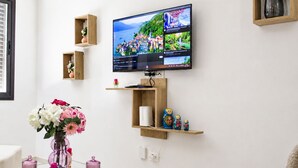 A living room with a flat-screen TV mounted on the wall, a glass coffee table with decorative items, and wooden shelves with various objects. - Bright, refined apartment in La Marsa (Marsa)