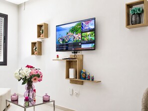 Ein Wohnzimmer mit einem flachbildfernseher an der Wand, einem Glastisch mit Dekoration und Holzregalen mit verschiedenen Gegenständen.