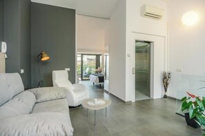 A modern living room with a sofa, a chair, a small table, and a lamp. There is a door leading to another room. - Penthouse overlooking the Dali Museum - Serena Stays (Figueres)