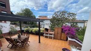 Eine Terrasse mit Tisch und Stühlen, einem Grill und Blumentöpfen.