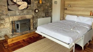 Ein Schlafzimmer mit Kamin aus Stein, einem Bett mit weißer Bettwäsche und einem hölzernen Kopfteil.