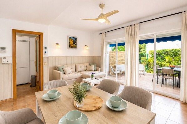 A modern living room with a sofa, dining table, and chairs, a ceiling fan, and a view of the outdoors.