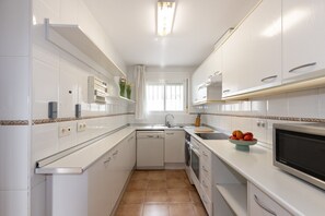 A compact kitchen with white cabinetry, a dishwasher, an oven, a microwave, and a sink.
