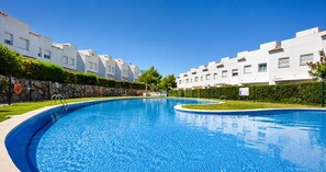 A swimming pool with a clear blue water, surrounded by white buildings and greenery.