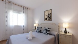 A neatly made bed with a rolled towel, two black and white patterned pillows, a bedside lamp, and a framed artwork on the wall.
