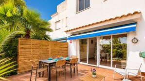A patio with a table and chairs, a wooden fence, and a building with a blue awning.