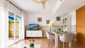 A modern living room with a TV, dining table, chairs, and a ceiling fan.