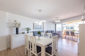 Een moderne keuken met witte kasten, een eettafel met stoelen, een potplant en uitzicht op een balkon.
