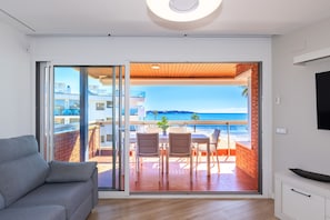 Een moderne woonkamer met een bank, een eethoek met stoelen en een tafel, en een schuifpui die leidt naar een balkon met uitzicht op zee.