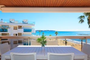 Een balkon met uitzicht op het strand en de oceaan, een tafel met stoelen en een potplant.