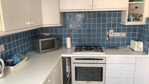 A compact kitchen with white cabinets, a microwave, a gas stove, and a toaster. - Kent Apartment 2 bed in Sandwich, With Free Parking (Sandwich)