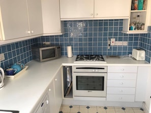 A compact kitchen with white cabinets, a microwave, a gas stove, and a toaster. - Kent Apartment 2 bed in Sandwich, With Free Parking (Sandwich)