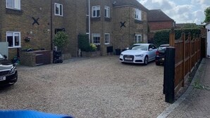 A residential building with a gravel driveway, a white car parked in the driveway, and a wooden fence along the side. - Kent Apartment 2 bed in Sandwich, With Free Parking (Sandwich)