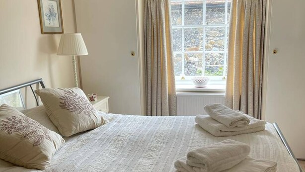 A neatly made bed with pillows and folded towels, a bedside lamp, and a window with curtains. - Kent Apartment 2 bed in Sandwich, With Free Parking (Sandwich)