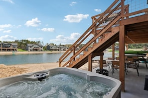 Un jacuzzi con terraza de madera y escaleras que dan a un área techada con vista al lago.