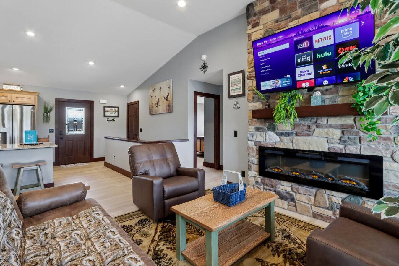 A living room with a stone fireplace, a mounted TV displaying streaming services, and a comfortable seating area.