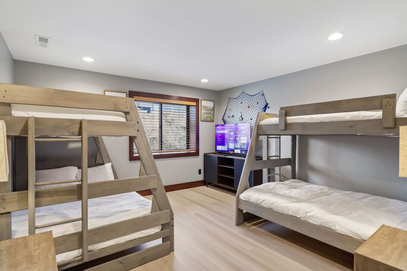 A room with bunk beds, a window with blinds, a TV, and a wall-mounted shelf.