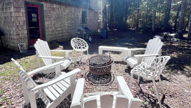 A stone building with a red door, surrounded by a forest. There are four white Adirondack chairs arranged around a fire pit. - Comfy 4BR Home on the Quietside [KelleyTown House] (Tremont)
