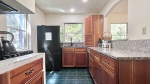 A kitchen with wooden cabinets, a black refrigerator, a granite countertop, and a tiled floor. - Comfy 4BR Home on the Quietside [KelleyTown House] (Tremont)