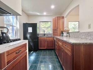 A kitchen with wooden cabinets, a black refrigerator, a granite countertop, and a tiled floor. - Comfy 4BR Home on the Quietside [KelleyTown House] (Tremont)