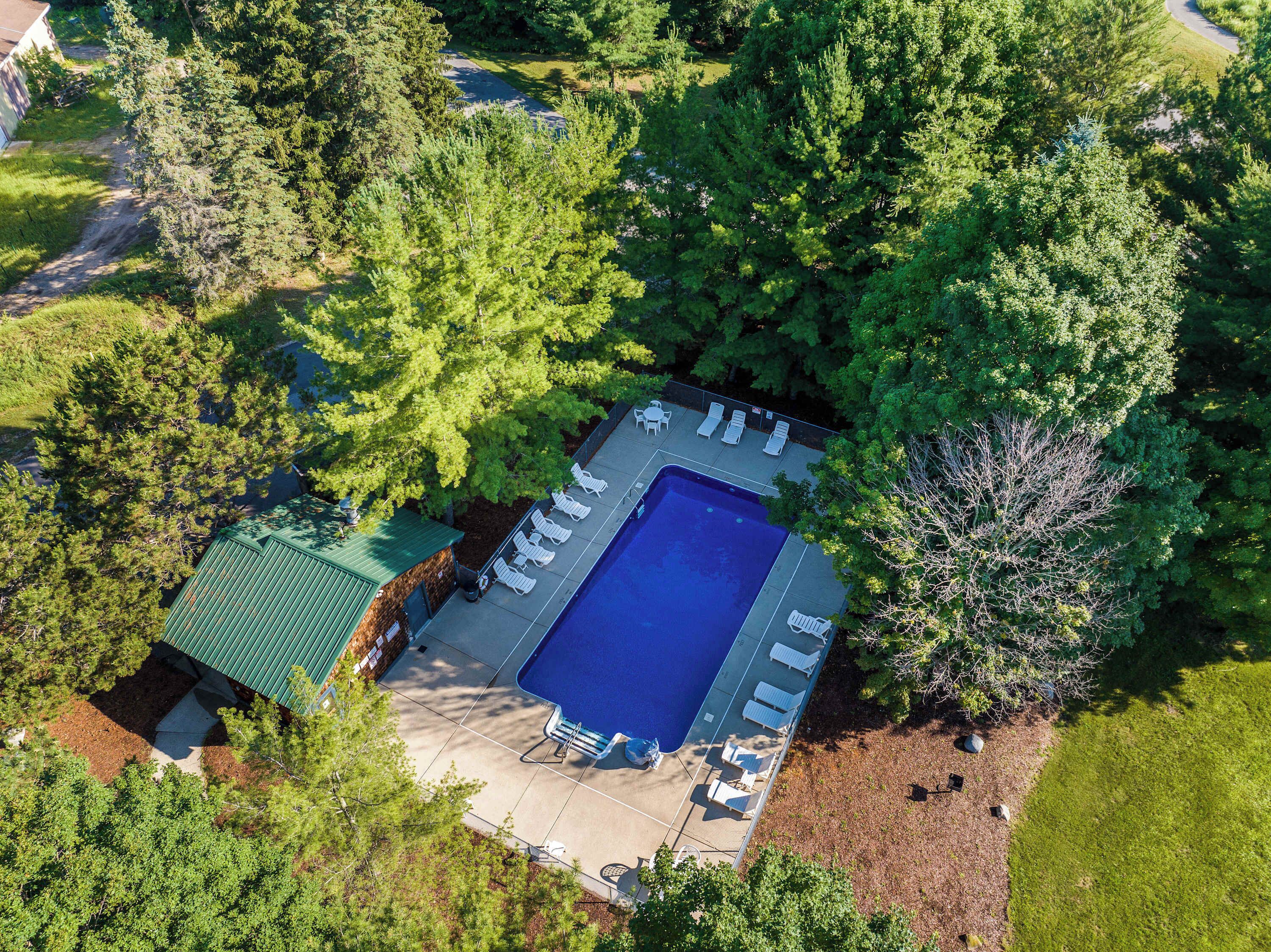 An aerial view of a residential property with a swimming pool, lounge chairs, and a green-roofed building.