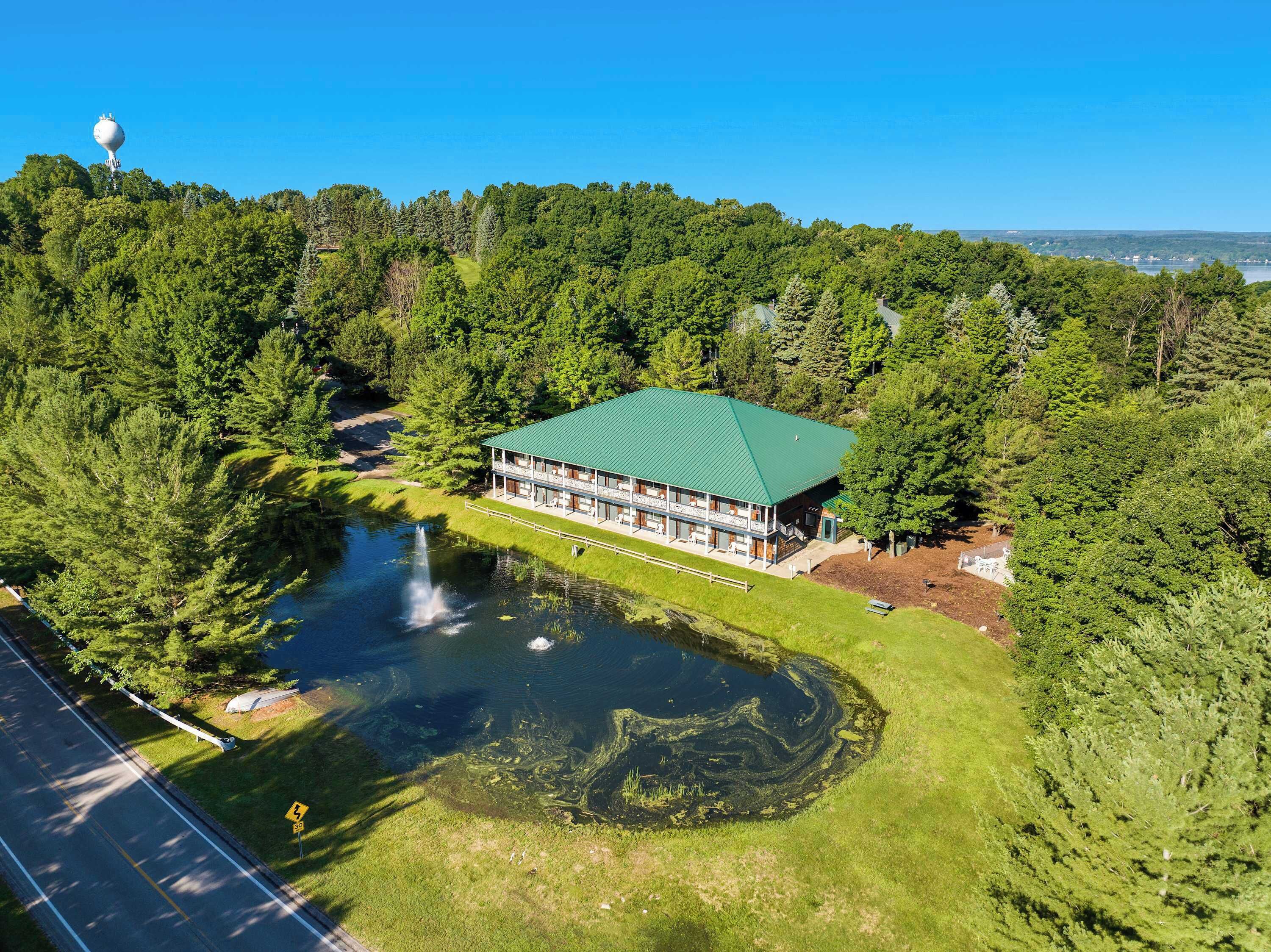 Eine Lodge mit Gründach, umgeben von dichtem Wald und einem Teich mit Wasserfall.