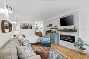 A modern living room with a sofa, ottoman, and a TV mounted on the wall. - Shanty Creek Condo, King Bed, Pool & Beach (Bellaire)