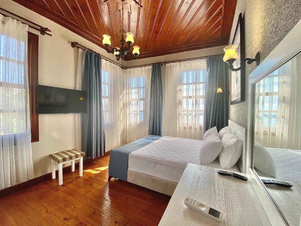 A bedroom with a bed, a bench, a TV, and a window with curtains.