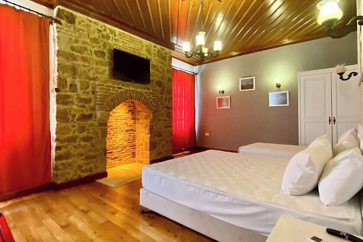 A bedroom with a stone wall, wooden ceiling, a bed, a TV, and a wardrobe.