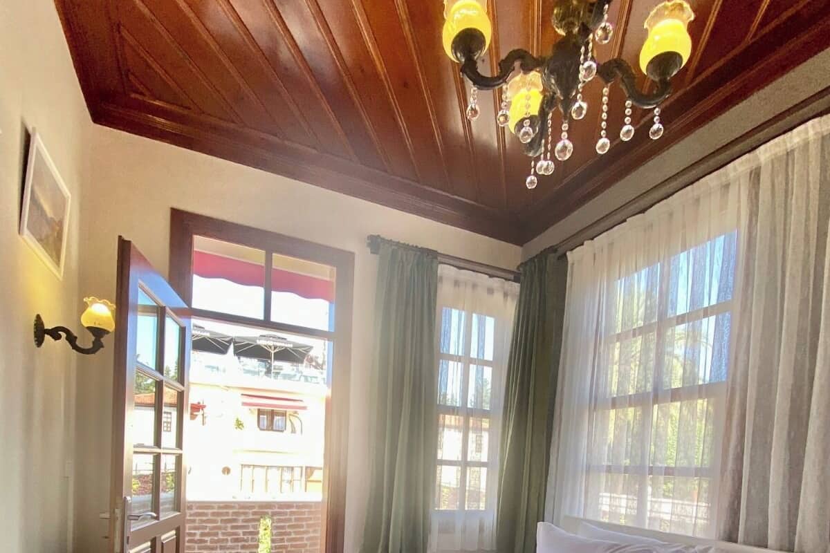 A bedroom with a large bed, wooden ceiling, and a view through a door to an outdoor area.