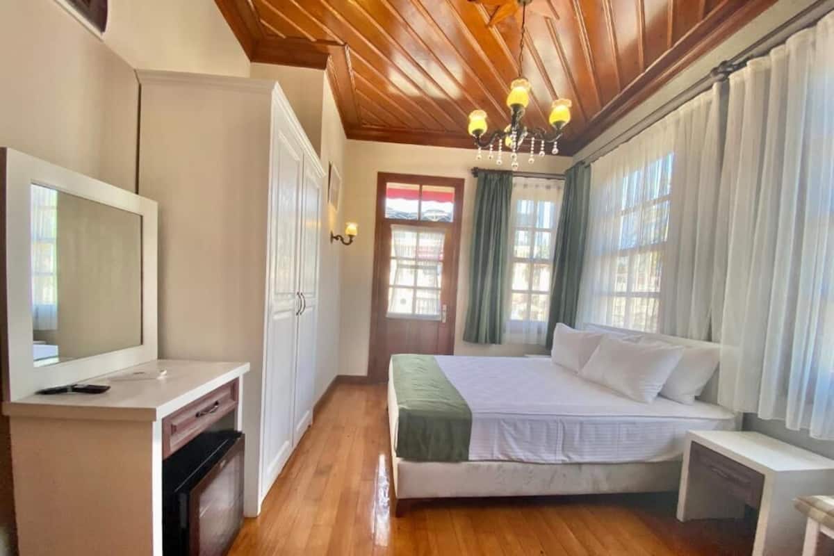 A bedroom with a bed, bedside table, a television, and a window with curtains.