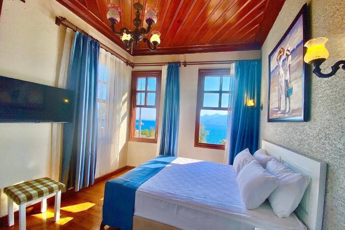 A bedroom with a bed, a bench, a TV, and windows with curtains.