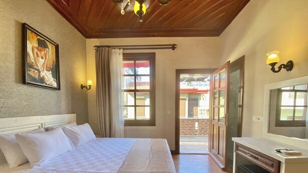 A hotel room with a bed, a desk with a computer, a painting on the wall, and a view through an open door. - Ulivo Hotel (Antalya)