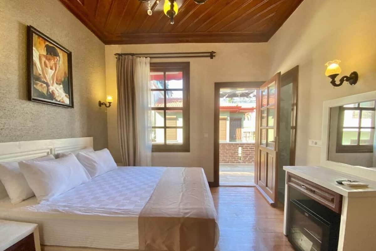 A bedroom with a bed, a desk with a computer, a fireplace, and a view of the outside.