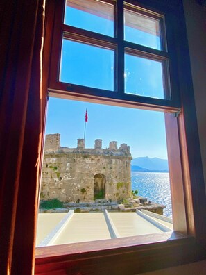 A window view of a castle with a flag, a clear sky, and a body of water. - Ulivo Hotel (Antalya)