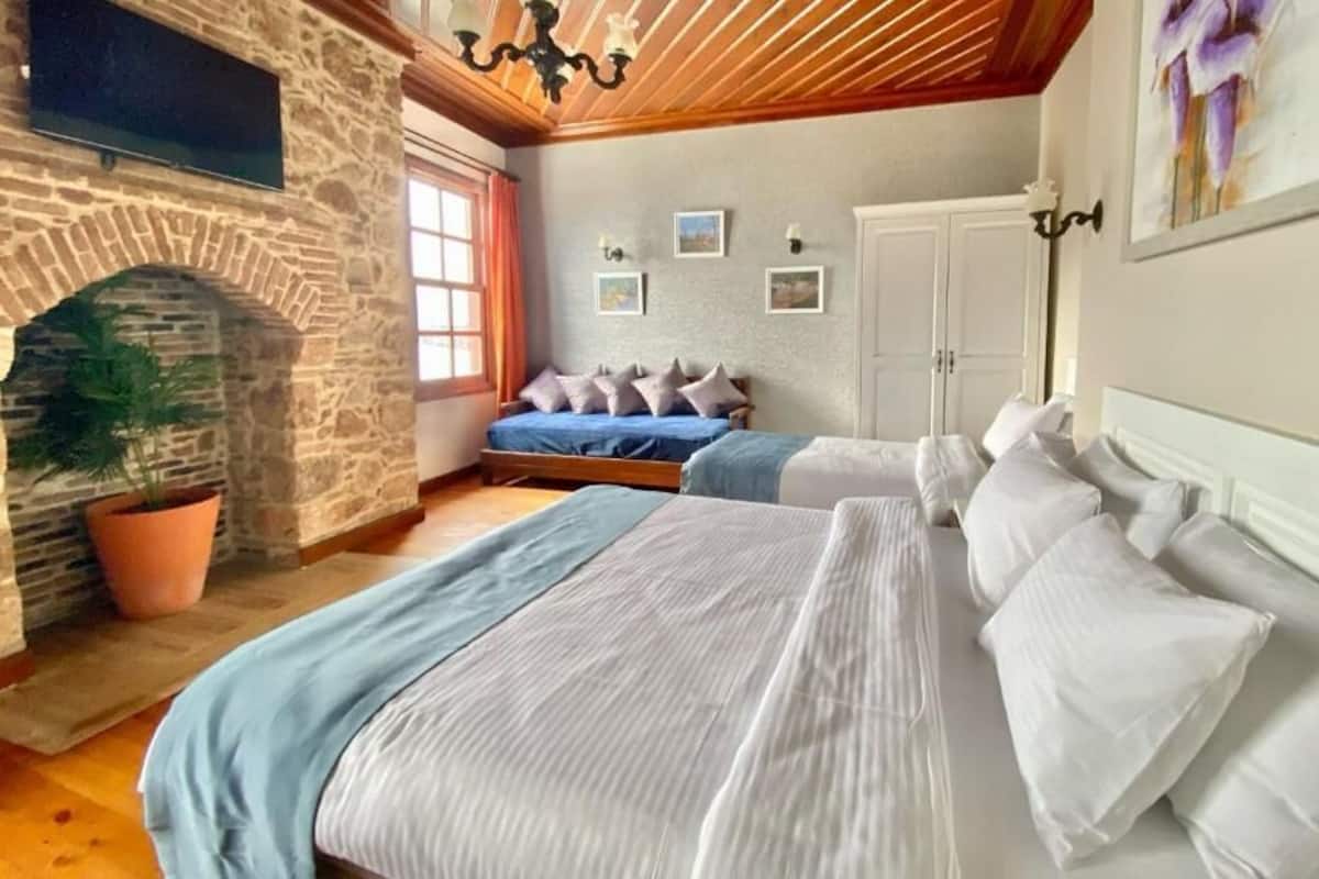 A bedroom with a stone fireplace, two beds, a potted plant, and a painting on the wall.